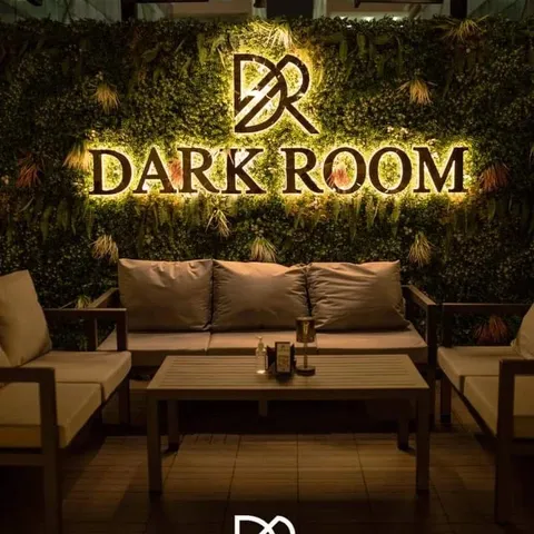 Illuminated Dark Room sign on a green plant wall above lounge seating at Dark Room Dubai Night Club